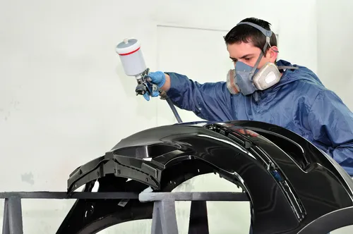 Spray painter applying paint to a car bumper in a spray booth